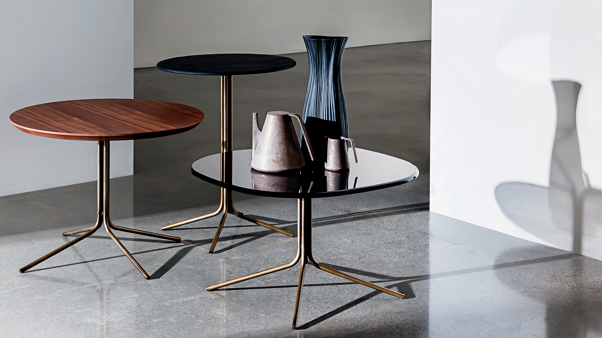 Tre tavolini rotondi in diverse altezze con base in metallo brunito e piano legno noce canaletto, ceramica colore nero e vetro colore nero