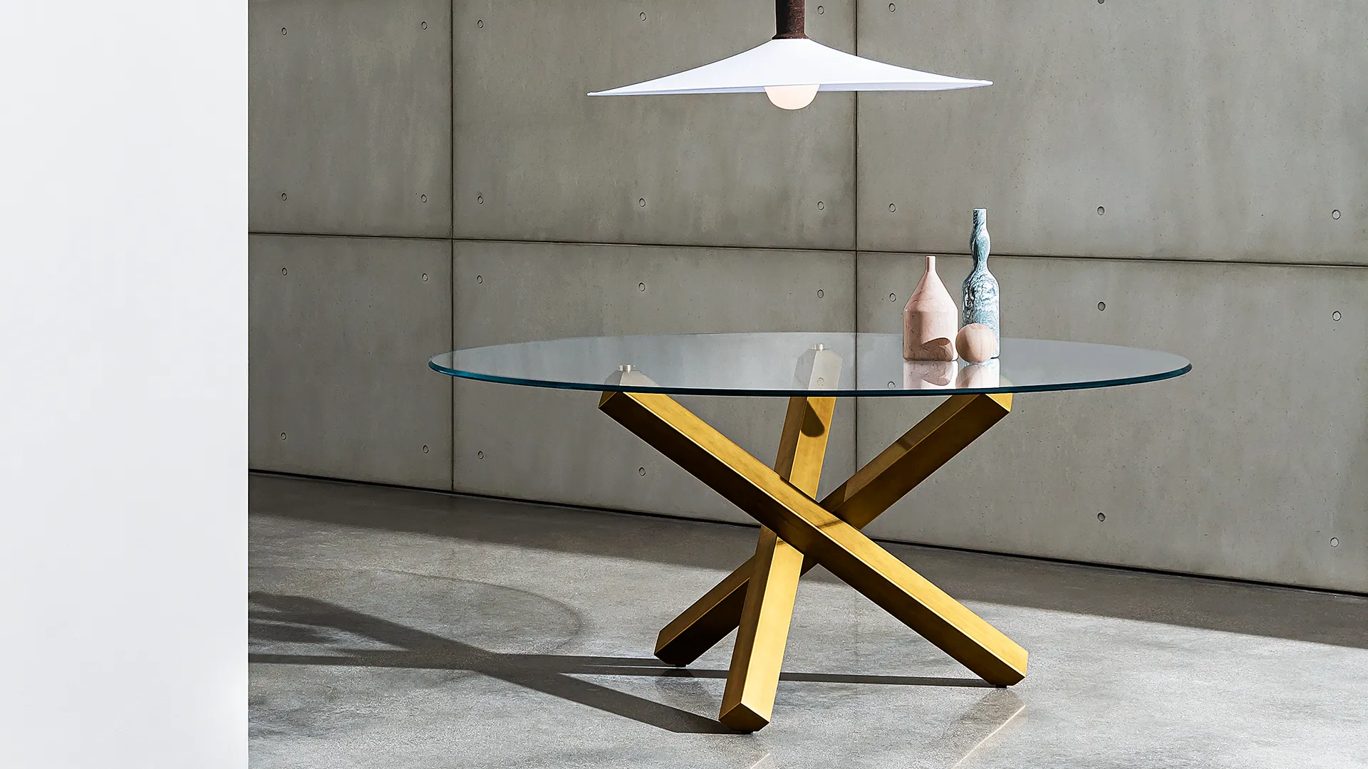 Tavolo rotondo moderno con base in metallo brunito composta da tre elementi incrociati e piano in vetro