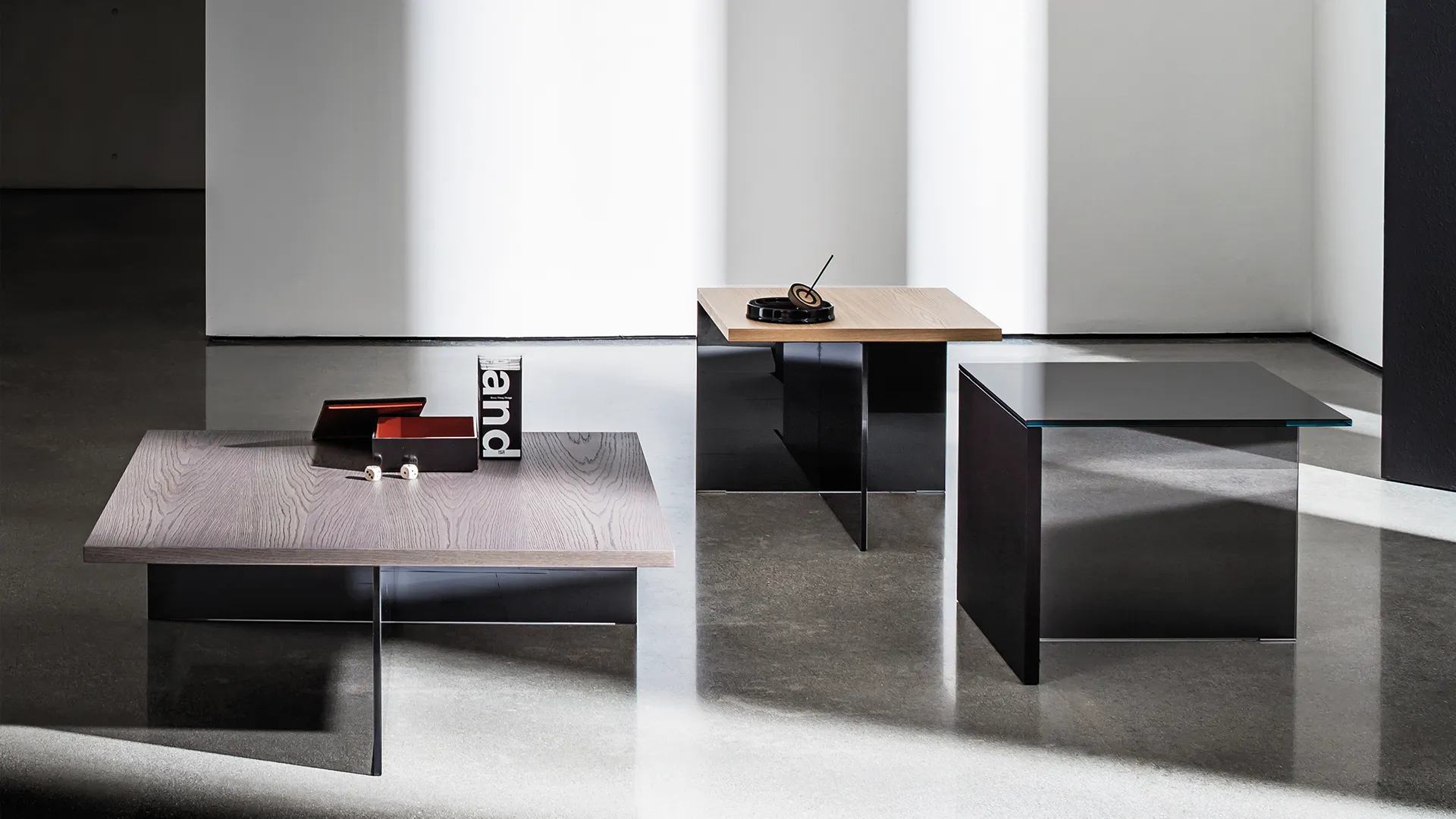 Tre tavolini quadrati in diverse dimensioni con base composta da un elemento in vetro fumé e un elemento in vetro stratificato nero con piano in legno