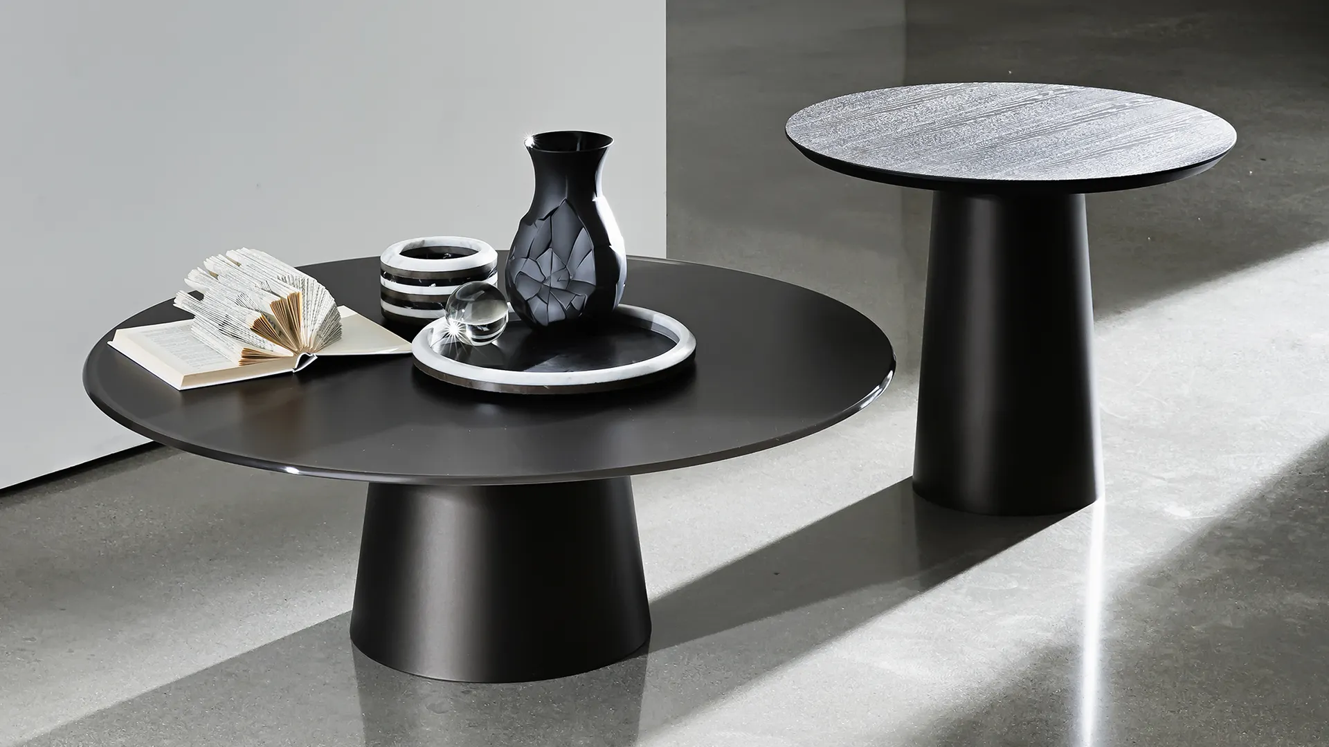 Due tavolini rotondi con base in metallo laccato colore caffè e piano in vetro laccato caffè e legno rovere tinto wengè