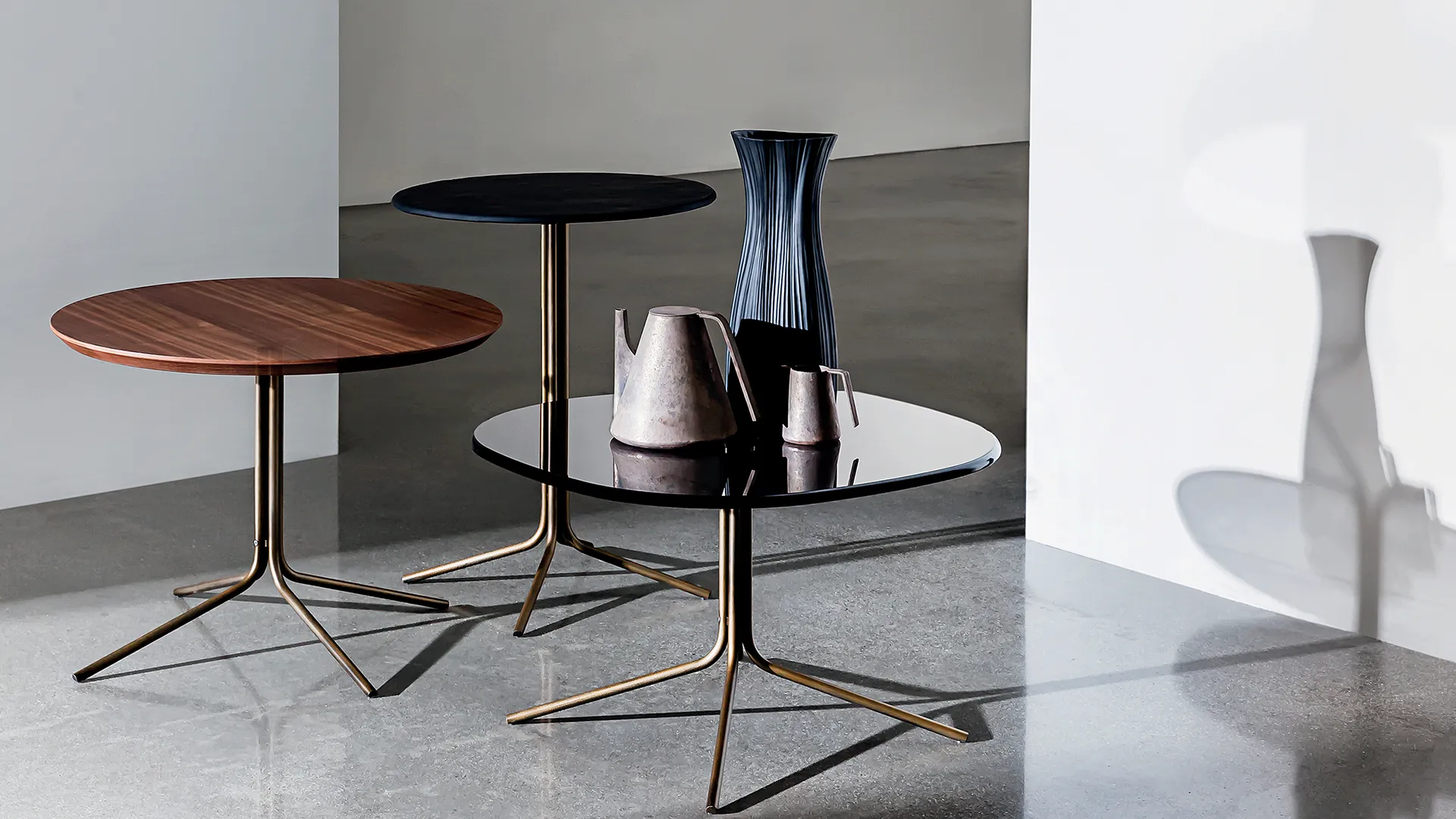 Tre tavolini rotondi in diverse dimensioni con base in metallo brunito e piano legno noce canaletto, ceramica colore nero e vetro colore nero
