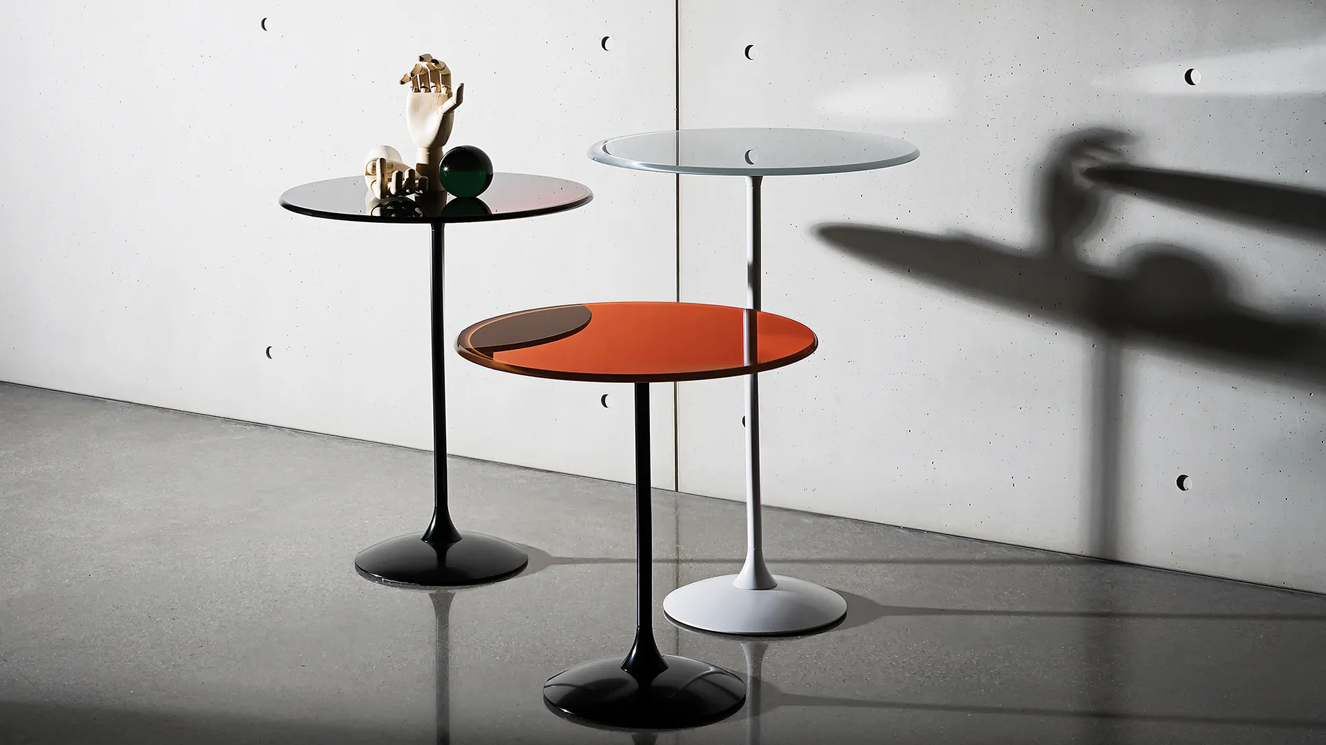 Tre tavolini rotondi a diverse altezze con base in metallo nero e piano in vetro ruggine e nero e base in metallo bianco con piano in vetro colore cem
